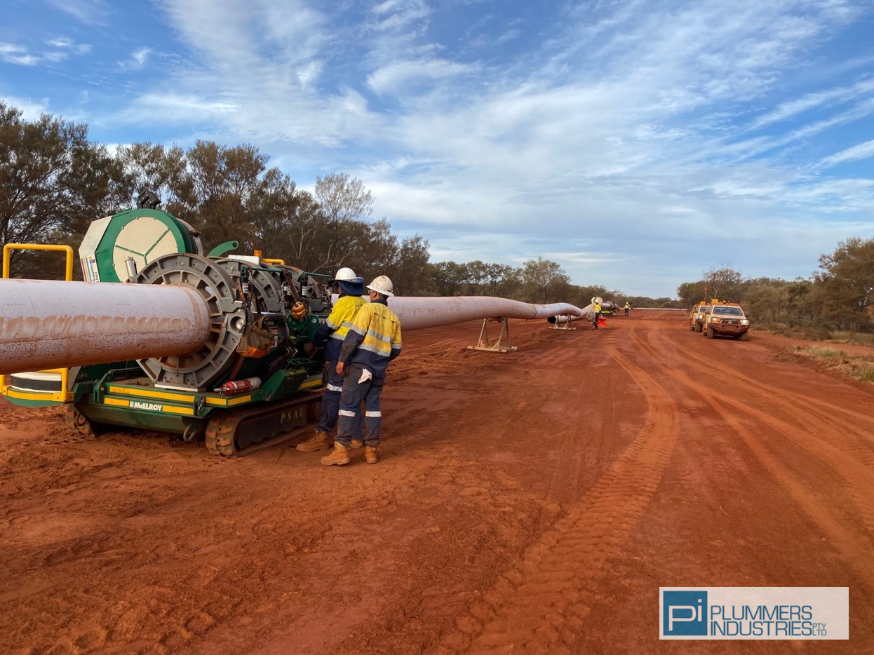 A worker stands beside a massive pipe on a dirt road, overseeing civil engineering projects.