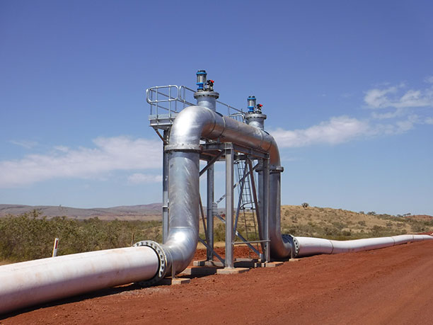 A wide infrastructure pipeline with dual valves positioned alongside a road.