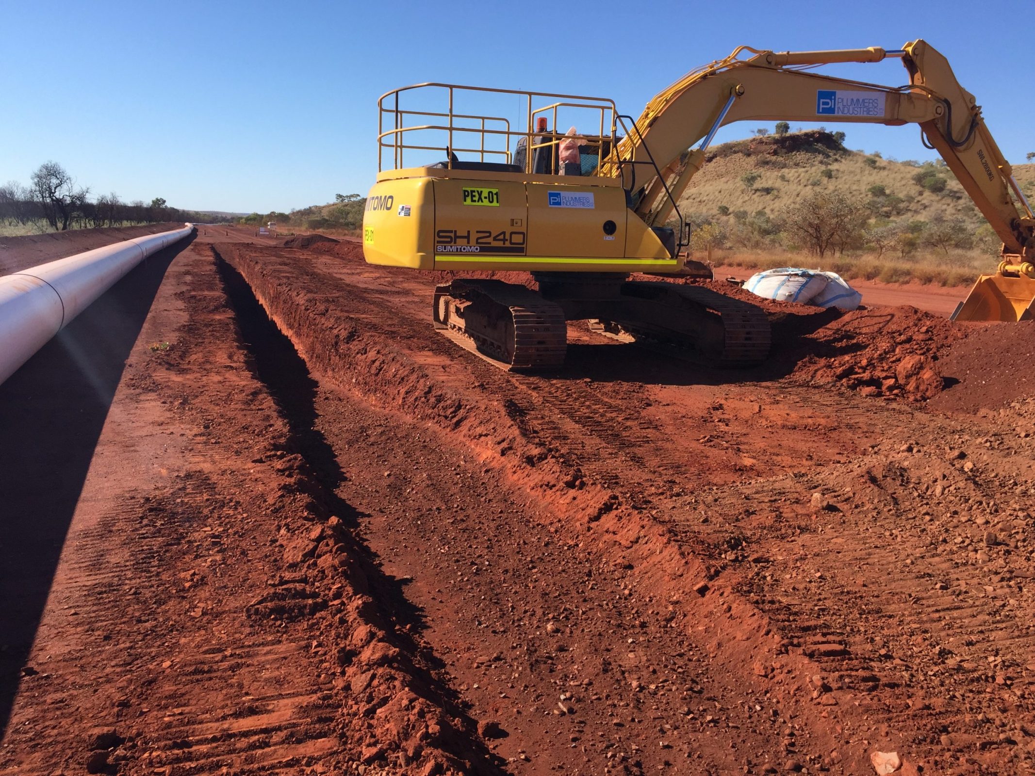 A yellow excavator is busy working on a road as part of an infrastructure pipeline project.