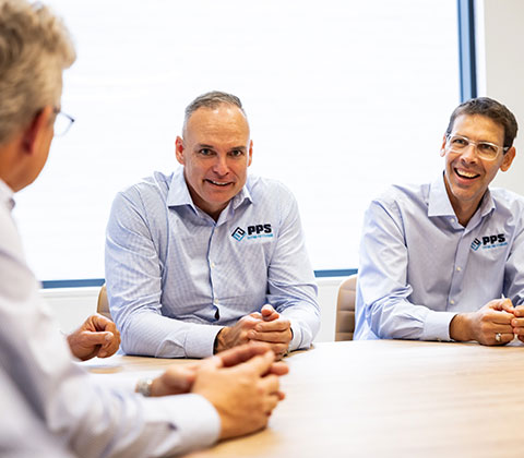 Three men sitting at a conference table, smiling, discussing piping solutions.
